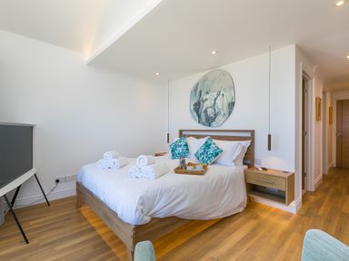 A bedroom with a wooden bed with white bedding and blue pillows a wooden floor and bedside table at Turquarze in Carbis Bay