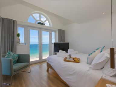 A bedroom with a bed, armchair, television, and large windows overlooking the sea at Turquarze in Carbis Bay