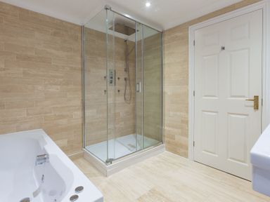 A bathroom with a glass shower enclosure a white bathtub a white door and beige tiled walls and floor at Turquarze Carbis Bay
