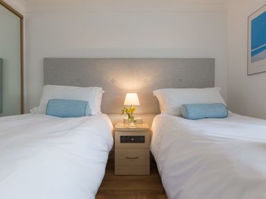 A bedroom with two single beds a nightstand with a lamp and flowers at Turquarze in Carbis Bay