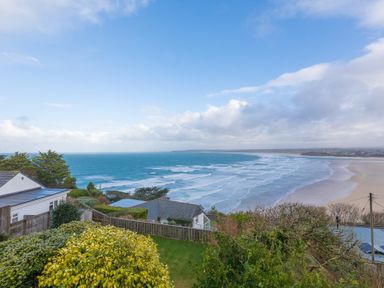 A coastal view with houses, trees, and waves on the beach at Whitsunday House in Carbis Bay
