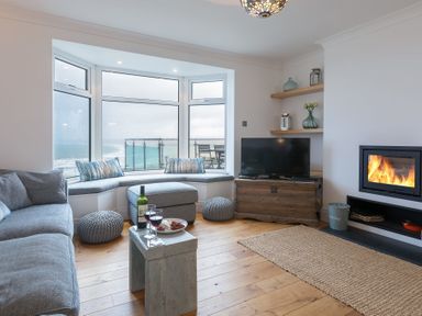 A living room with a grey sofa, bay window seat, TV on a wooden chest, fireplace, and wooden floor at Whitsunday House in Carbis Bay
