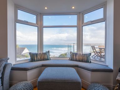 A seating area with cushions by a large bay window overlooking the sea at Whitsunday House in Carbis Bay
