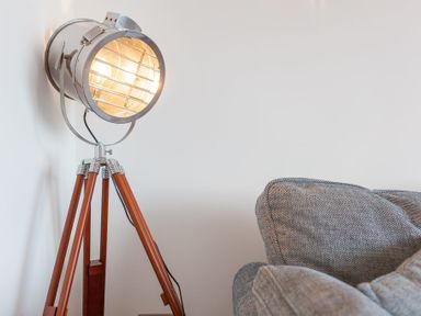 A floor lamp with a metal spotlight head and wooden tripod legs next to a gray fabric sofa at Whitsunday House in Carbis Bay