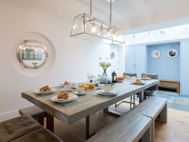 A dining room with a wooden table set for breakfast and benches at Whitsunday House in Carbis Bay