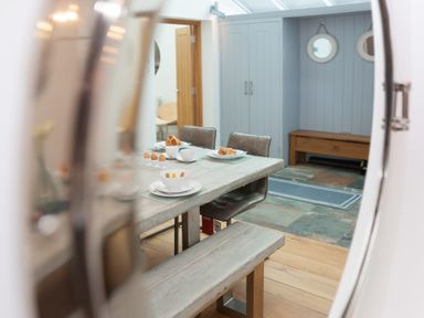 A dining area with a wooden table set with plates cups eggs and croissants next to grey chairs and a bench at Whitsunday House in Carbis Bay