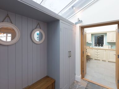 A hallway with two round mirrors and a wooden bench leading to a kitchen with cream cabinets at Whitsunday House in Carbis Bay