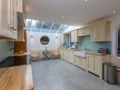 A kitchen with cream cabinets wooden countertops a round window two chairs a small table and a skylight at Whitsunday House in Carbis Bay