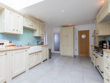 A kitchen with cream cabinets blue tile backsplash and wooden countertops at Whitsunday House in Carbis Bay