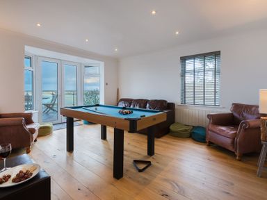 A room with a pool table in the center surrounded by leather armchairs and a sofa with a window and glass doors overlooking a balcony at Whitsunday House in Carbis Bay