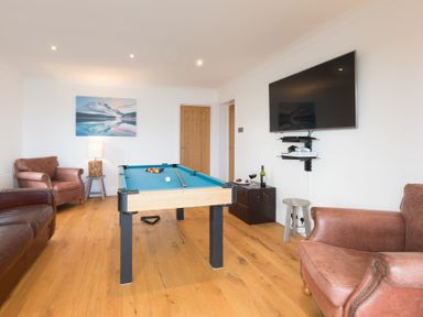 A game room with a pool table leather armchairs a wall-mounted television and wooden doors at Whitsunday House in Carbis Bay