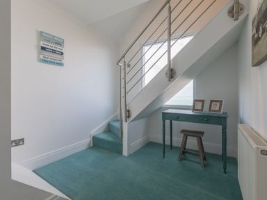 A staircase with teal carpet and a small table under the stairs with two picture frames at Whitsunday House in Carbis Bay