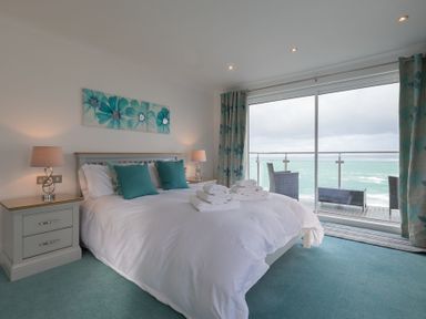A bedroom with a large bed and folded towels by a glass balcony overlooking the sea at Whitsunday House in Carbis Bay