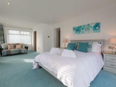 A bedroom with a bed with white bedding and teal pillows and a sofa with cushions near a window at Whitsunday House in Carbis Bay