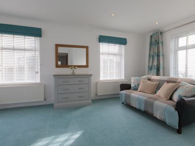 A sitting room with a sofa a chest of drawers and windows with blinds at Whitsunday House in Carbis Bay