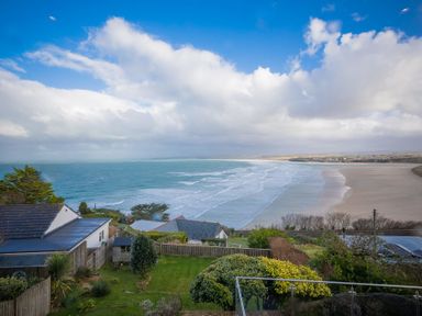 A garden with trees and houses overlooking a beach and ocean under a cloudy sky at Whitsunday House in Carbis Bay
