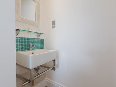 A bathroom sink with a faucet a glass shelf with toiletry bottles a mirror and teal mosaic tiles at Whitsunday House in Carbis Bay