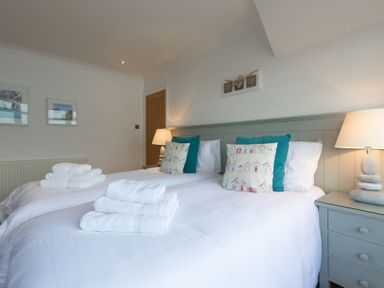 A bedroom with two single beds with white linens pillows and folded towels bedside tables with lamps at Whitsunday House in Carbis Bay