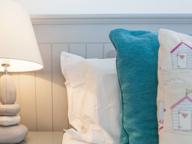 A bedside table with a lamp next to a bed with white and blue cushions at Whitsunday House in Carbis Bay