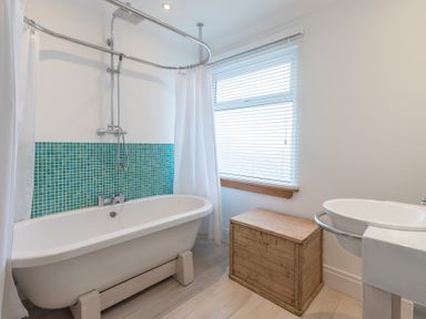 A bathroom with a white bathtub teal tile backsplash wooden chest and a white sink at Whitsunday House in Carbis Bay