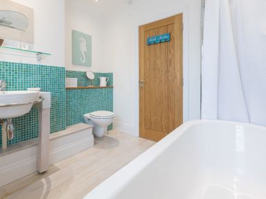 A bathroom with a bathtub sink toilet wooden door and turquoise tiled wall at Whitsunday House in Carbis Bay