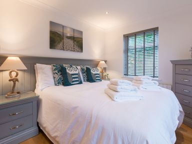 A bedroom with a double bed with pillows and folded towels nightstands with lamps and a window with blinds at Whitsunday House in Carbis Bay
