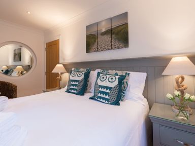 A bedroom with a double bed two owl patterned pillows bedside tables with lamps and a three panel beach artwork at Whitsunday House in Carbis Bay