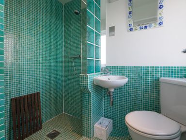 A bathroom with green tiled shower and walls a white sink and toilet at Whitsunday House in Carbis Bay