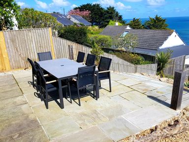 An outdoor patio with a rectangular table and eight chairs overlooking houses and the sea at Whitsunday House in Carbis Bay