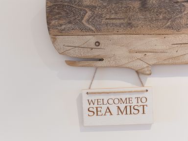 A wooden whale wall decoration with a hanging sign that says welcome to sea mist