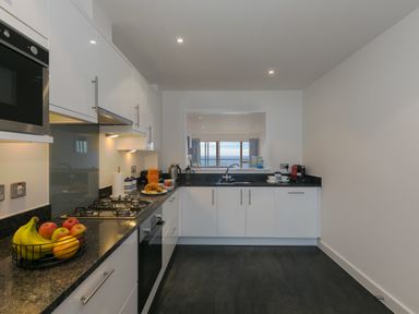 A kitchen with white cabinets black countertops fruit basket and a window overlooking the sea at Sea Mist in Carbis Bay