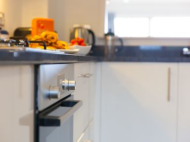 A kitchen countertop with a stovetop and oven below counters with pastries and fruit on the counter at Sea Mist in Carbis Bay