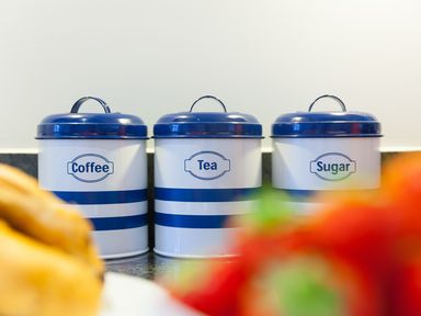 Three metal containers labeled coffee tea and sugar with blue lids on a kitchen counter at Sea Mist in Carbis Bay