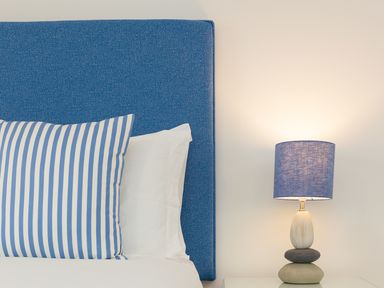 A bed with a blue headboard and striped pillow next to a lamp on a white bedside table