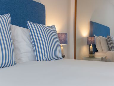 A bed with blue striped pillows blue headboard and a bedside table with a lamp at Sea Mist in Carbis Bay