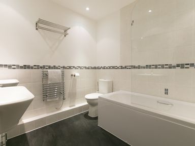 A bathroom with a bathtub with a glass screen a toilet a towel rack and a sink at Sea Mist in Carbis Bay