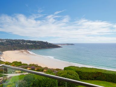 A view of a sandy beach with ocean waves and a green hillside at Sea Mist in Carbis Bay