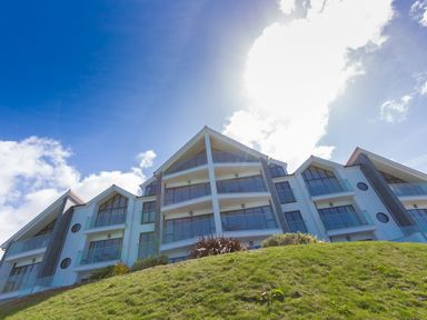 A modern multi-story building with glass balconies on a grassy hill under a blue sky at Sea Mist in Carbis Bay