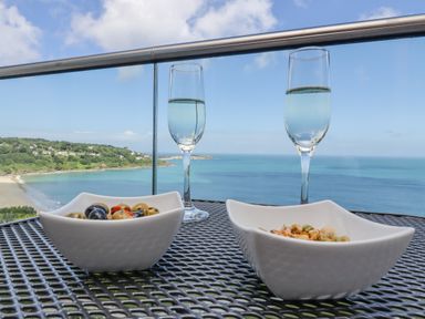 A balcony table with two bowls of snacks and two glasses of water overlooking a beach and ocean at Sea Mist in Carbis Bay