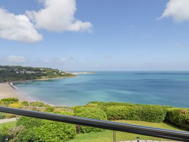A coastal view with a sandy beach green bushes and calm sea at Sea Mist in Carbis Bay