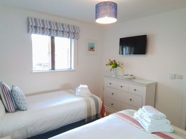 A bedroom with two single beds white dresser with flowers and a wall-mounted TV at Sea Mist in Carbis Bay