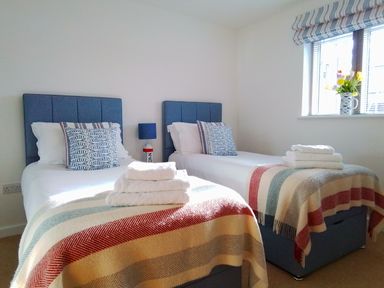 A bedroom with two single beds each with folded towels and a window with flowers at Sea Mist in Carbis Bay