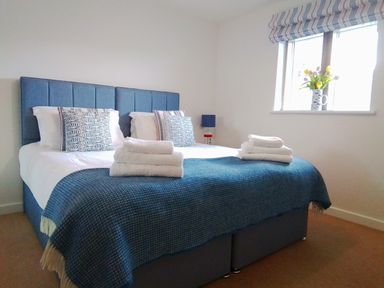 A bedroom with a bed blue headboard pillows folded towels and a window with flowers at Sea Mist in Carbis Bay