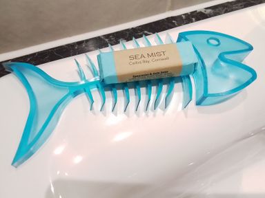 A blue fish-shaped soap holder with a bar of spearmint and kelp soap labeled Sea Mist Carbis Bay Cornwall