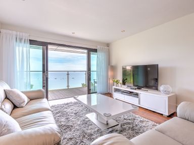 A living room with leather sofas a white coffee table a TV on a stand and a view of the sea at Abalone in St Ives