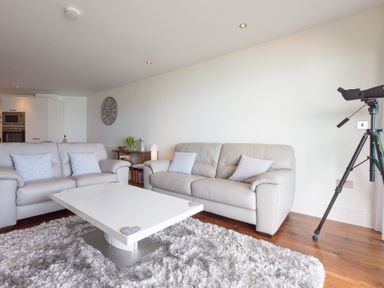A living room with two sofas a white coffee table a telescope and a wall clock at Abalone in St Ives