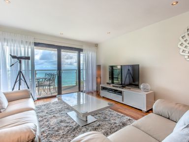 A living room with leather sofas a coffee table a television and a telescope by sliding glass doors overlooking the sea at Abalone in St Ives