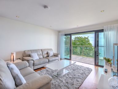 A living room with gray sofas a white coffee table a rug and a balcony with glass doors at Abalone in St Ives