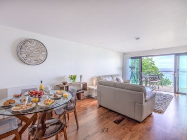 A dining table set with breakfast items and a living room with sofas and a balcony overlooking the sea at Abalone in St Ives