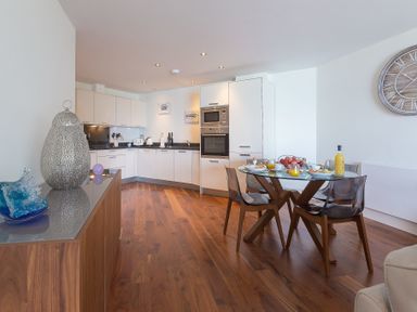 A kitchen with white cabinets and a glass dining table with four chairs at Abalone in St Ives
